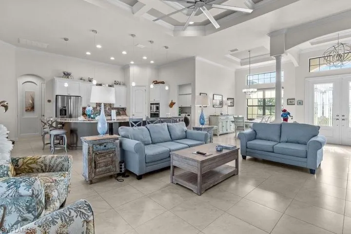 Tiled living room featuring french doors, coffered ceiling, ceiling fan with notable chandelier, a towering ceiling, and ornamental molding