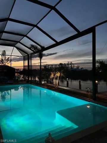 Pool at dusk featuring a lanai and a water view