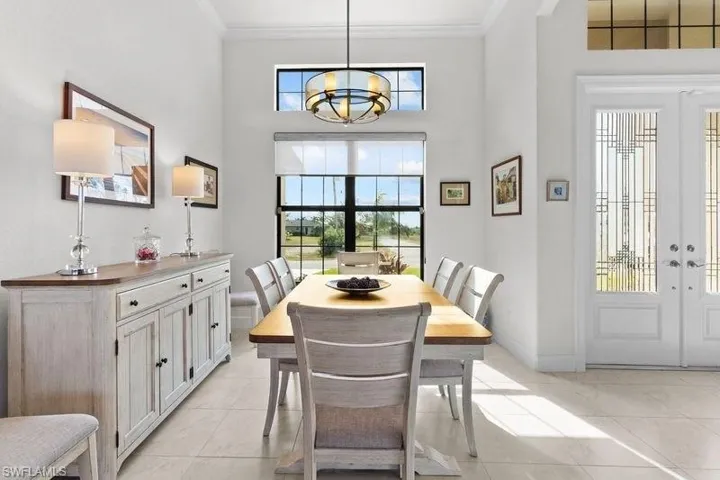 Dining space featuring french doors, crown molding, a towering ceiling, a chandelier, and light tile patterned floors