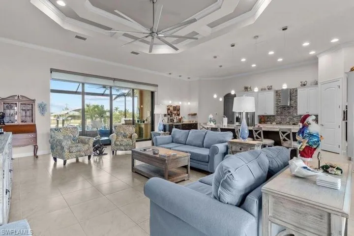Living room with a tray ceiling, ceiling fan, crown molding, and light tile patterned flooring
