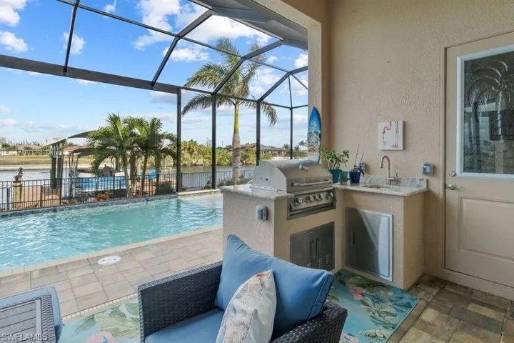 View of pool featuring grilling area, an outdoor kitchen, sink, a lanai, and a patio
