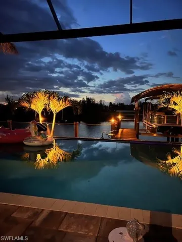 Pool at dusk with a lanai, a water view, and a boat dock