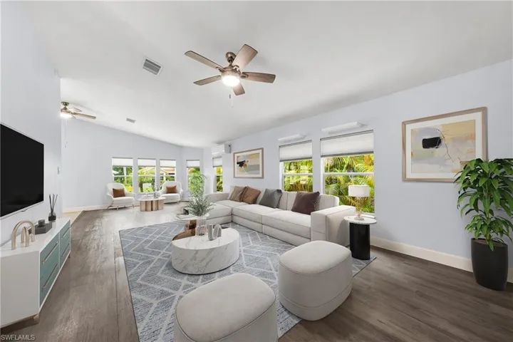 Spacious living area featuring vaulted ceilings, wood-finish flooring, multiple windows providing abundant light, and ceiling fans
