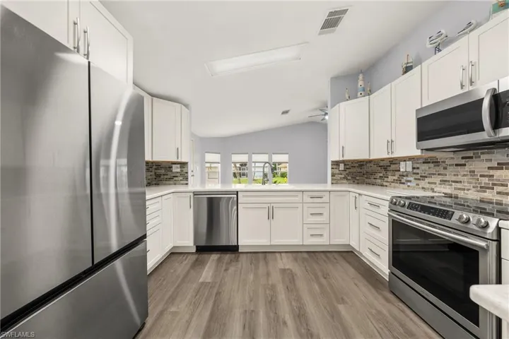 Kitchen with white shaker cabinetry, stainless steel appliances, and wood-finish flooring