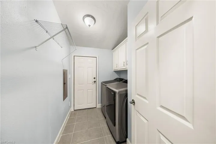 Laundry area featuring tiled flooring, white cabinetry, overhead lighting, and a wire shelving unit