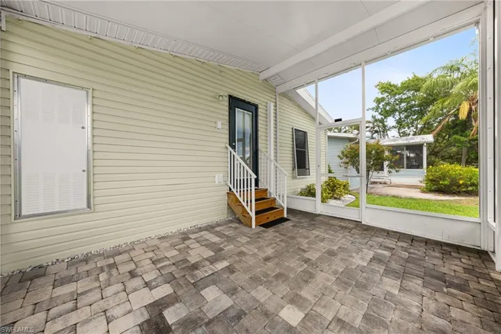 Screened patio featuring paver flooring, a white railing, and a dark-paneled door