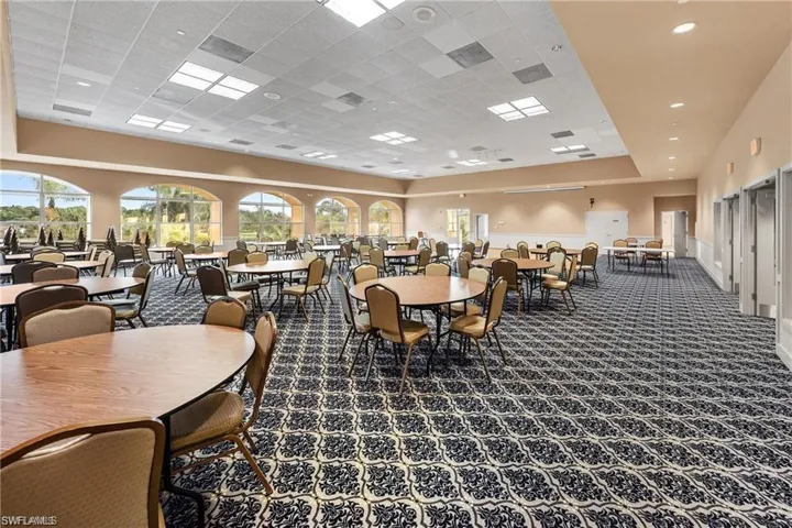 Spacious gathering area featuring expansive arched windows, patterned carpet flooring, recessed lighting, and a neutral wall palette