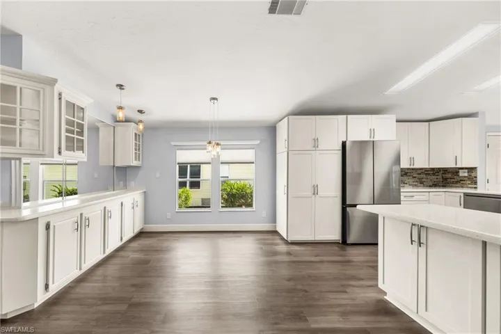 Open-concept kitchen featuring white cabinetry, light countertops, wood-finish flooring, a stainless steel refrigerator, and pendant lighting