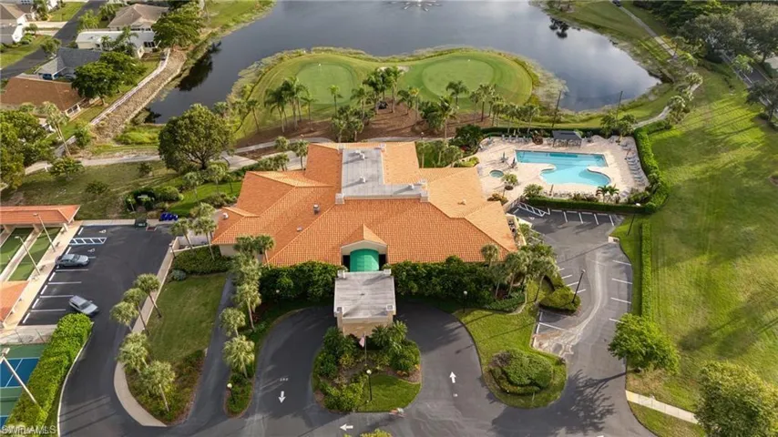 Clubhouse building featuring a terracotta tile roof, large parking areas, and surrounding manicured landscaping