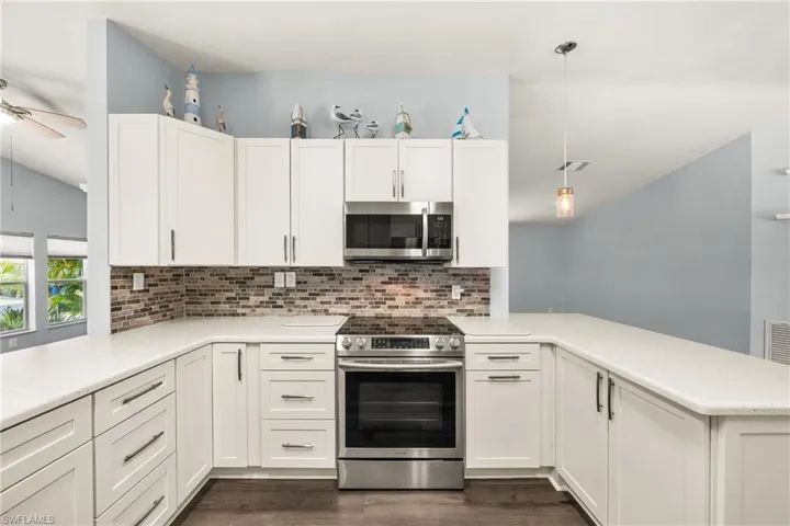 Modern kitchen featuring white shaker cabinetry, stainless steel appliances, a multi-tone tile backsplash, and light-toned countertops
