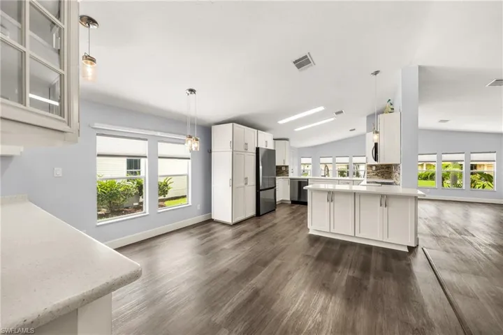 Open-concept kitchen and dining area featuring wood-finish flooring, white cabinetry, integrated appliances, and pendant lighting