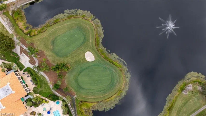 Aerial perspective showcasing a golf course with two greens and a sand trap bordered by a body of water with a water feature