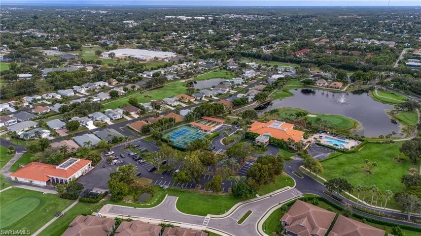 Aerial perspective showcasing the community's amenities, including a central lake with a water feature, multiple tennis courts, and a community pool