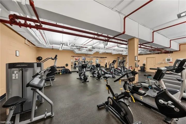 Fitness center featuring multiple exercise machines, exposed red piping, and a mirrored wall