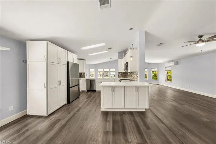 Open-concept kitchen featuring white cabinetry, stainless steel appliances, a central island, wood-finish flooring, and vaulted ceilings
