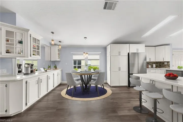 Bright kitchen featuring white cabinetry, stainless steel appliances, wood-finish flooring, a kitchen island with seating, and a dedicated dining area