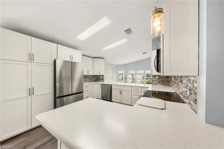 Kitchen featuring white shaker cabinetry, stainless steel appliances, light-toned countertops, a mosaic tile backsplash, and wood-finish flooring