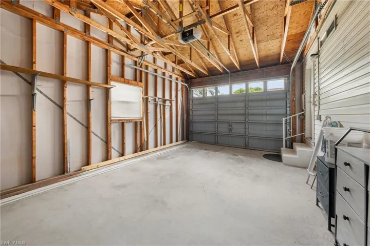 Spacious garage featuring a concrete floor, exposed wood ceiling beams, a metal garage door with upper windows, and an interior access door with a small landing