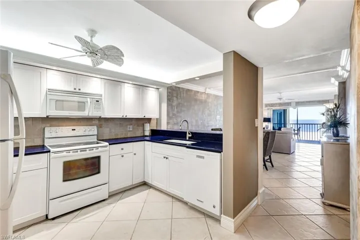Kitchen featuring a ceiling fan, white appliances, dark countertops, white cabinetry, and light tile patterned floors