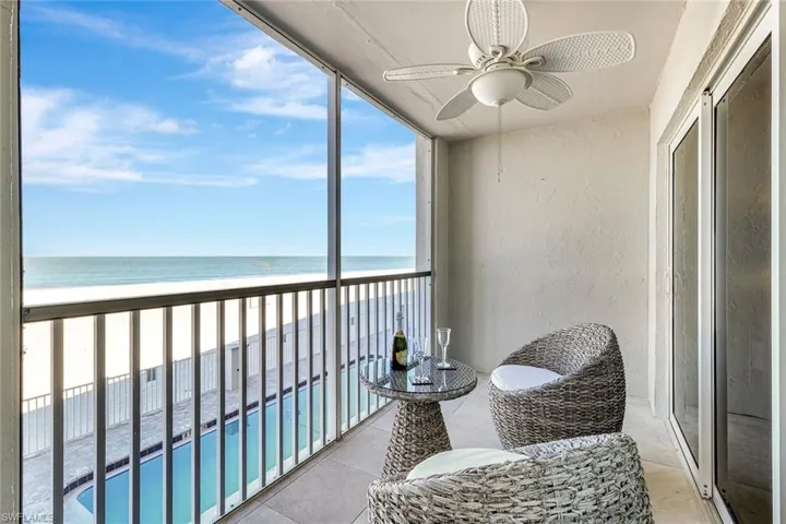 Balcony with a ceiling fan, view of water and beach, and view of pool