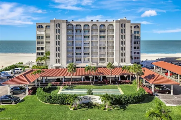 View of apartment building / complex with view of water and beach and uncovered parking