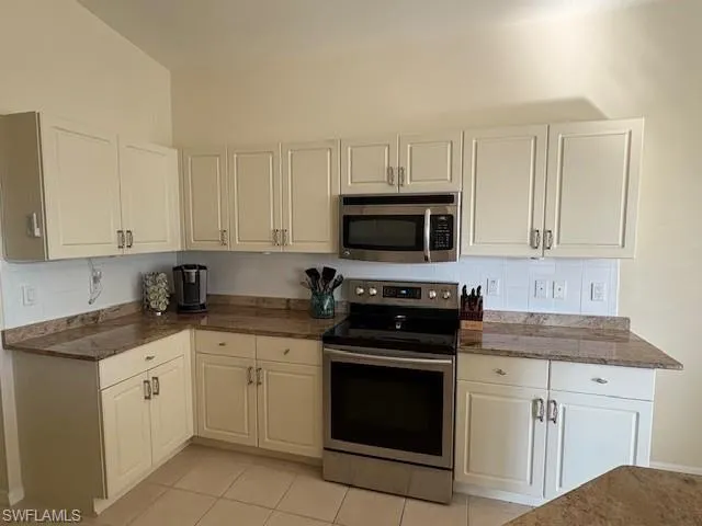 Kitchen featuring appliances with stainless steel finishes, dark stone countertops, light tile patterned floors, backsplash, and white cabinetry