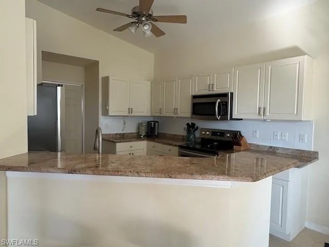 Kitchen with dark stone counters, stainless steel appliances, a peninsula, white cabinetry, and vaulted ceiling