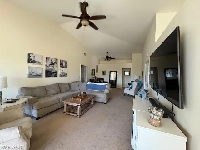 Living area featuring light colored carpet, a ceiling fan, and high vaulted ceiling