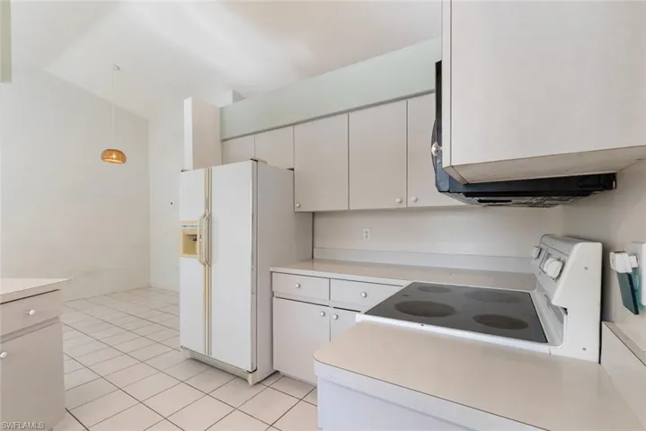Kitchen featuring stove, light tile floors, white cabinets, pendant lighting, and white refrigerator with ice dispenser