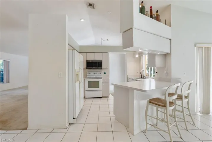 Kitchen with a breakfast bar, white appliances, white cabinets, and light tile floors