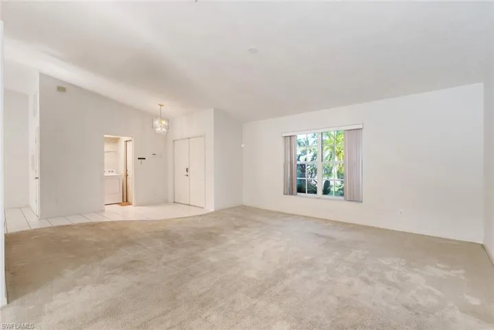 Spare room featuring light colored carpet, vaulted ceiling, washer / dryer, and an inviting chandelier