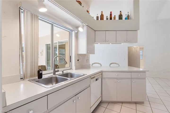 Kitchen featuring a wealth of natural light, sink, light tile flooring, and white dishwasher