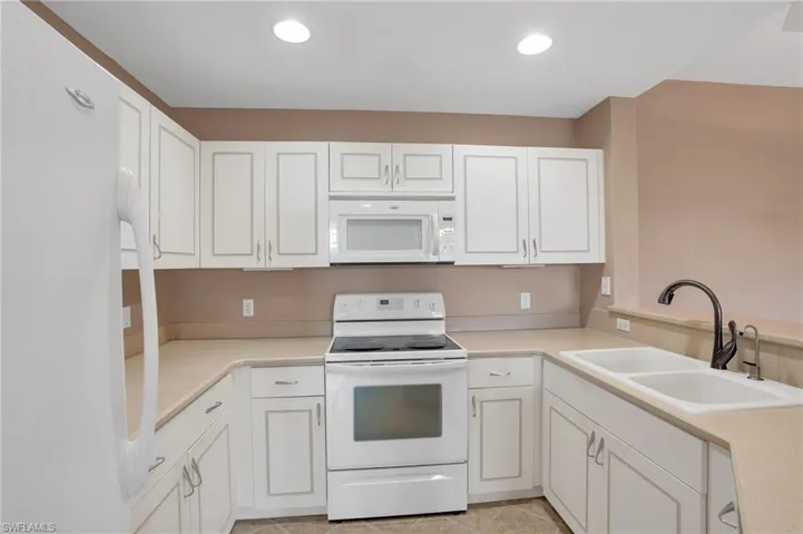 Kitchen featuring white cabinets, sink, white appliances, and light tile floors