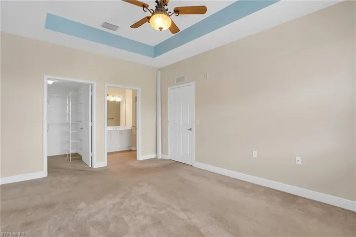 Unfurnished bedroom featuring a closet, ensuite bathroom, ceiling fan, a walk in closet, and light carpet