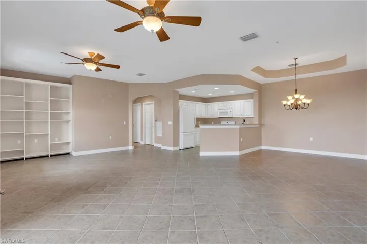 Unfurnished living room featuring light tile floors, a raised ceiling, and ceiling fan with notable chandelier
