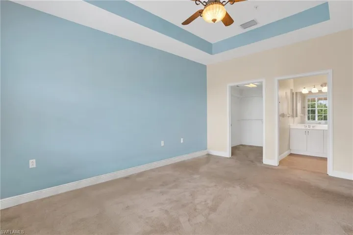 Unfurnished bedroom featuring a tray ceiling, a walk in closet, ceiling fan, and carpet floors