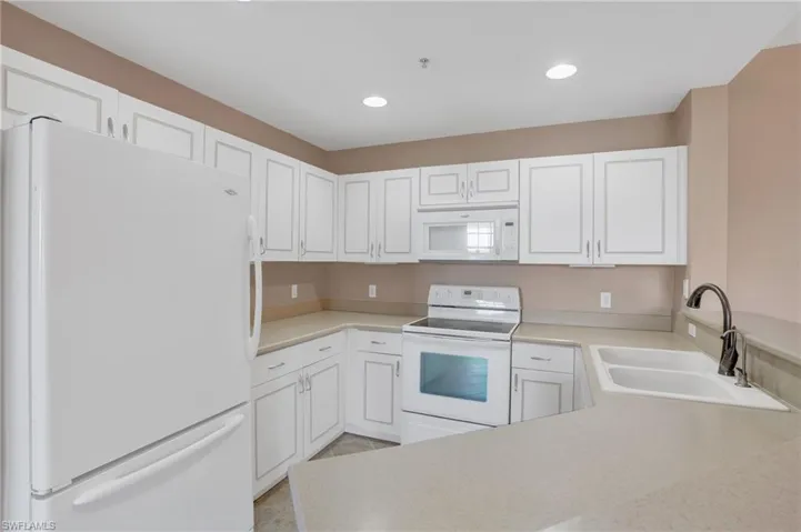 Kitchen with white appliances, sink, white cabinetry, and kitchen peninsula