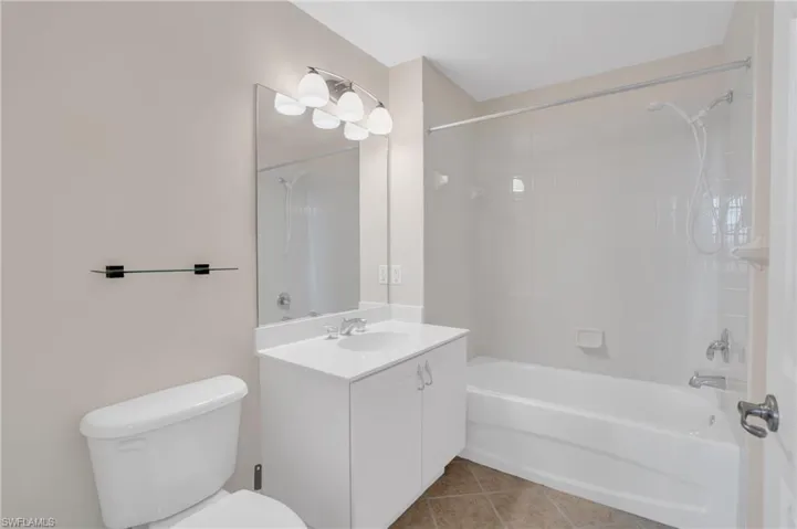 Full bathroom with tile flooring, toilet, tiled shower / bath combo, and large vanity