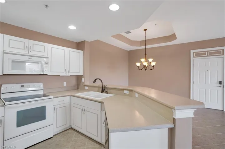 Kitchen featuring white appliances, white cabinets, kitchen peninsula, sink, and a raised ceiling