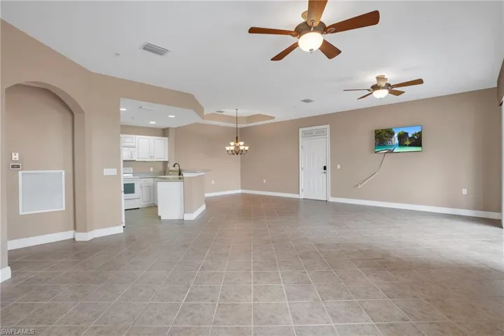 Tiled empty room with a tray ceiling, sink, and ceiling fan with notable chandelier