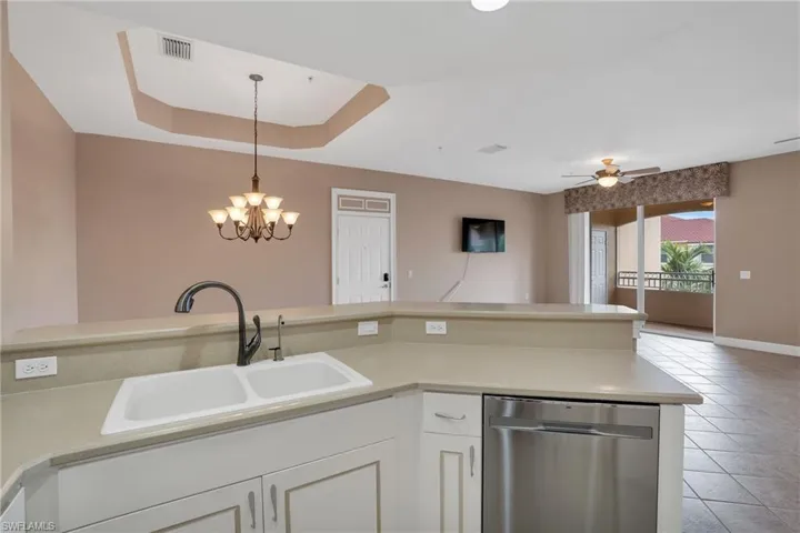 Kitchen featuring ceiling fan with notable chandelier, hanging light fixtures, a raised ceiling, stainless steel dishwasher, and sink