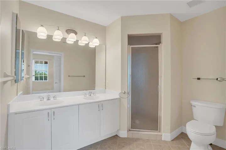 Bathroom with double sink, tile floors, oversized vanity, a shower with door, and toilet