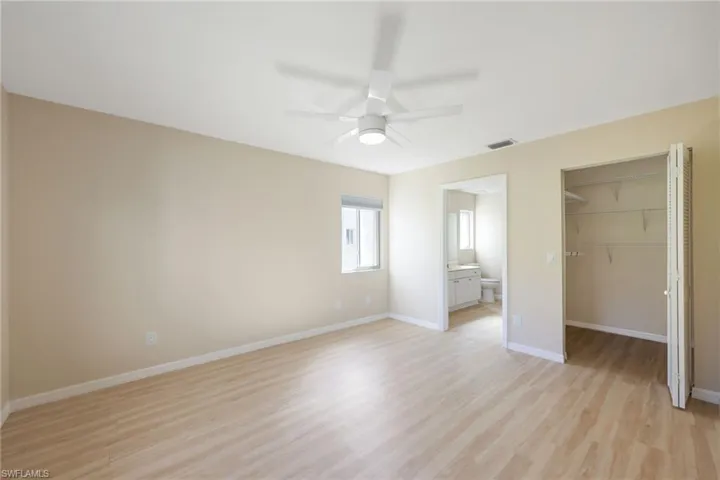 Unfurnished bedroom with a walk in closet, light wood-type flooring, ceiling fan, and ensuite bathroom