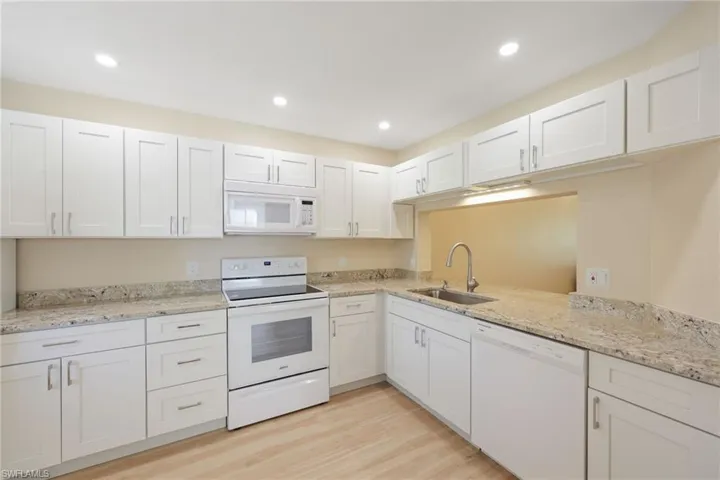 Kitchen featuring white appliances, white cabinets, light wood-style floors, light stone counters, and recessed lighting