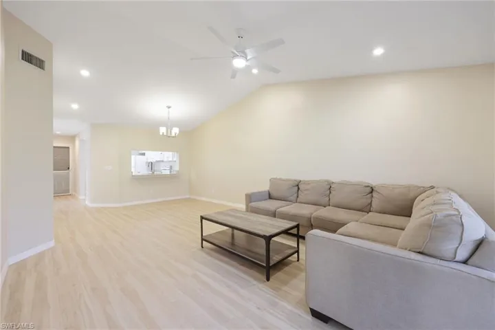 Living room with light wood-type flooring, a ceiling fan, vaulted ceiling, and hanging lights