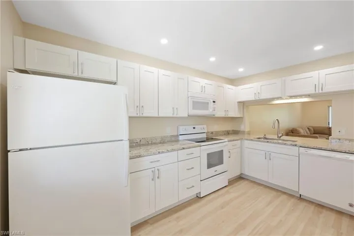 Kitchen featuring white appliances, white cabinetry, light wood-style floors, light stone countertops, and recessed lighting