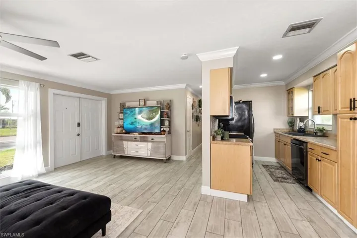 Kitchen featuring light countertops, light wood-style floors, crown molding, black dishwasher, and light brown cabinetry