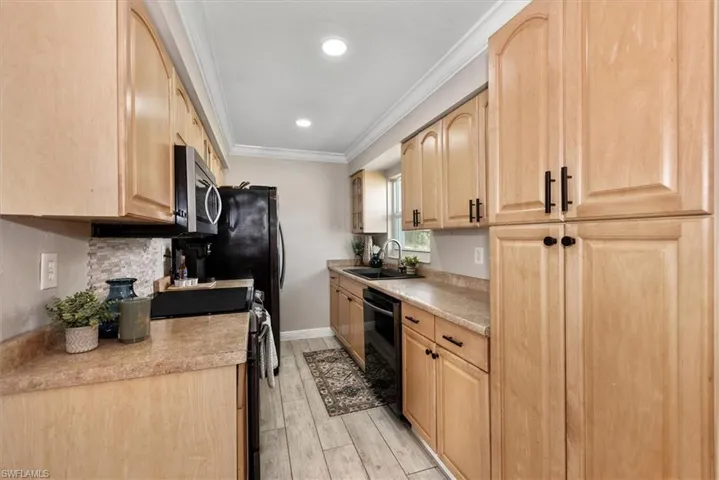 Kitchen with light brown cabinets, ornamental molding, stainless steel appliances, light countertops, and light wood-style floors