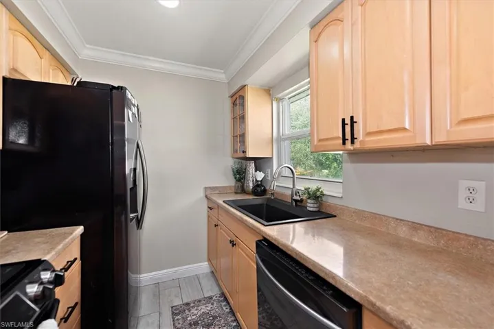 Kitchen featuring light brown cabinetry, crown molding, black appliances, glass insert cabinets, and light wood-type flooring