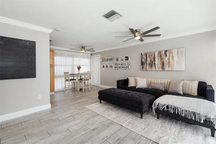 Living area featuring ornamental molding, light wood-style floors, and a ceiling fan